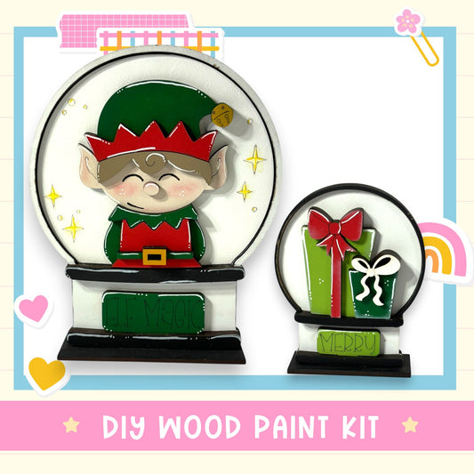 a DIY wood paint kit for creating a Christmas-themed snow globe. The kit includes a snow globe with a cartoon elf figure and a gift box, as well as a label that says "MERRY".
