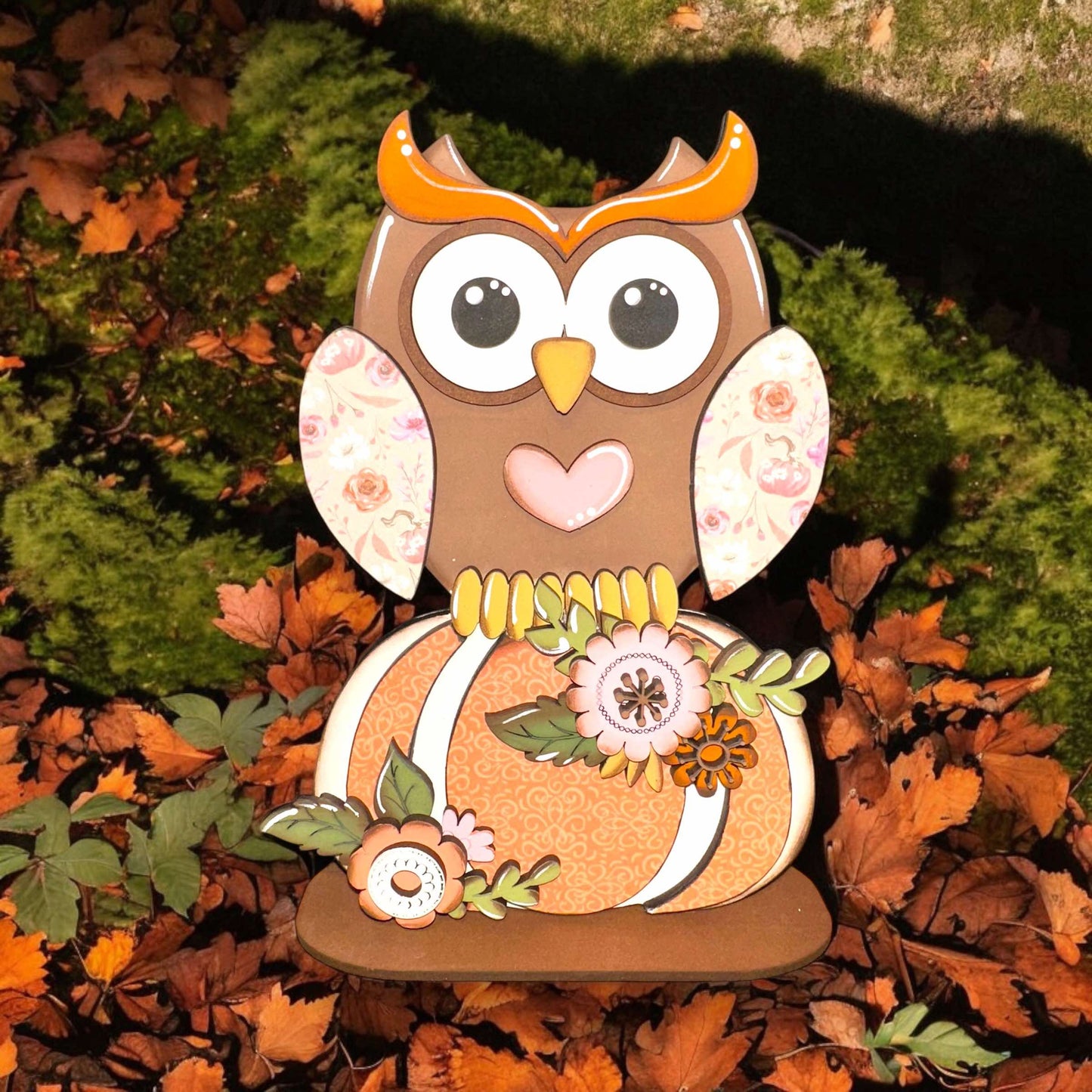 a wooden owl sitting on top of a pile of leaves