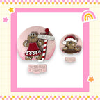 two gingerbread cookies, one larger and one smaller, both wearing festive hats and dressed in red and white outfits. The larger cookie is positioned on the left side of the image, while the smaller cookie is on the right side. The background of the image is pink, and there is a sign that reads "Gingerbread Bakery" in the center.