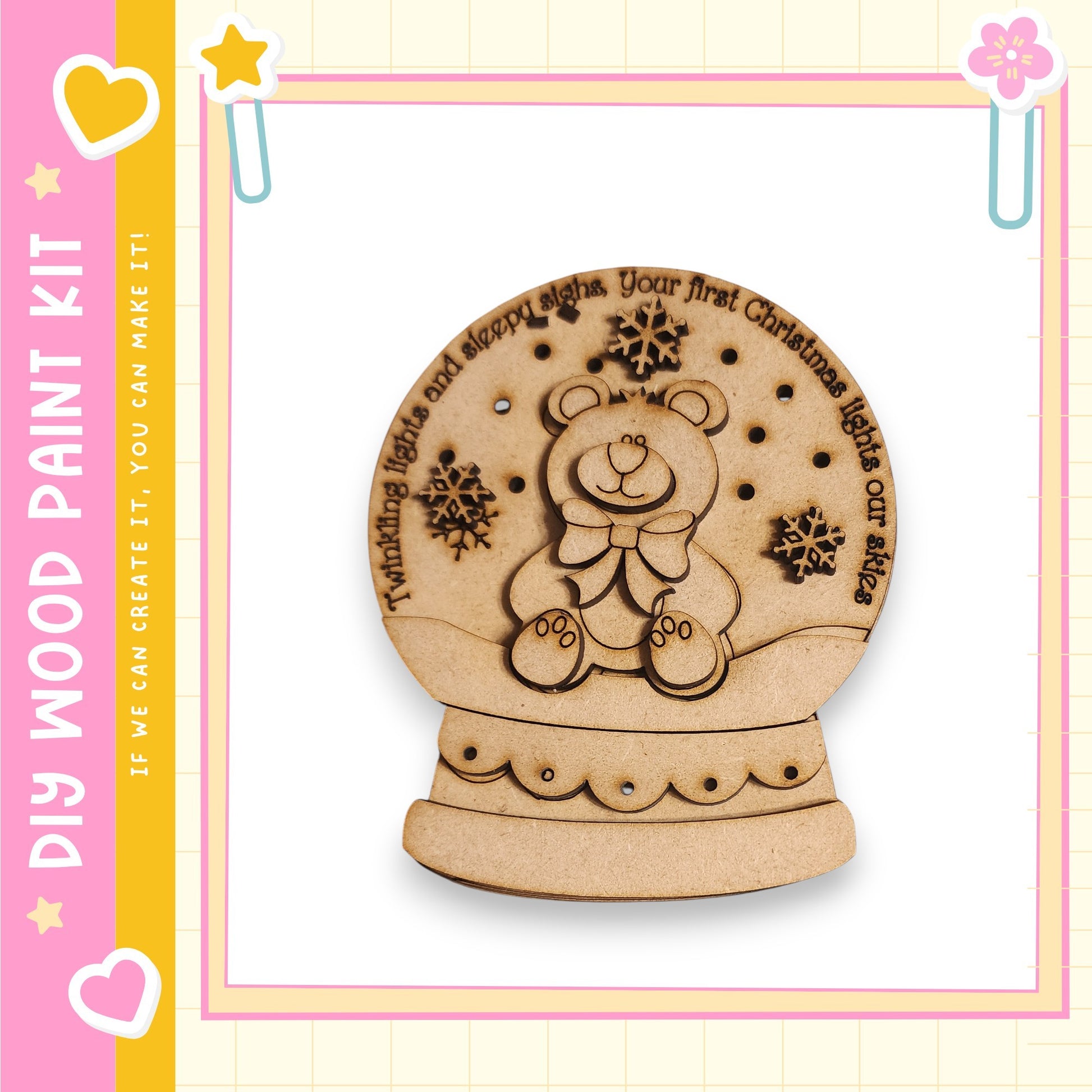 A wooden snow globe with a teddy bear design, surrounded by snowflakes, is displayed against a pink and yellow background.