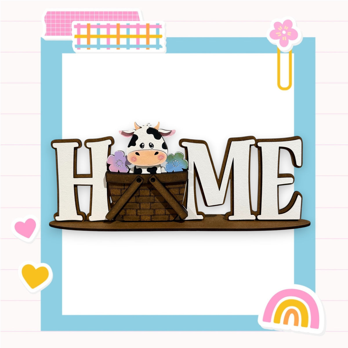 A wooden sign with the word "HOME" in large letters, featuring a cow sitting in a basket. The sign is surrounded by various colorful and whimsical elements, such as hearts, flowers, and a rainbow.