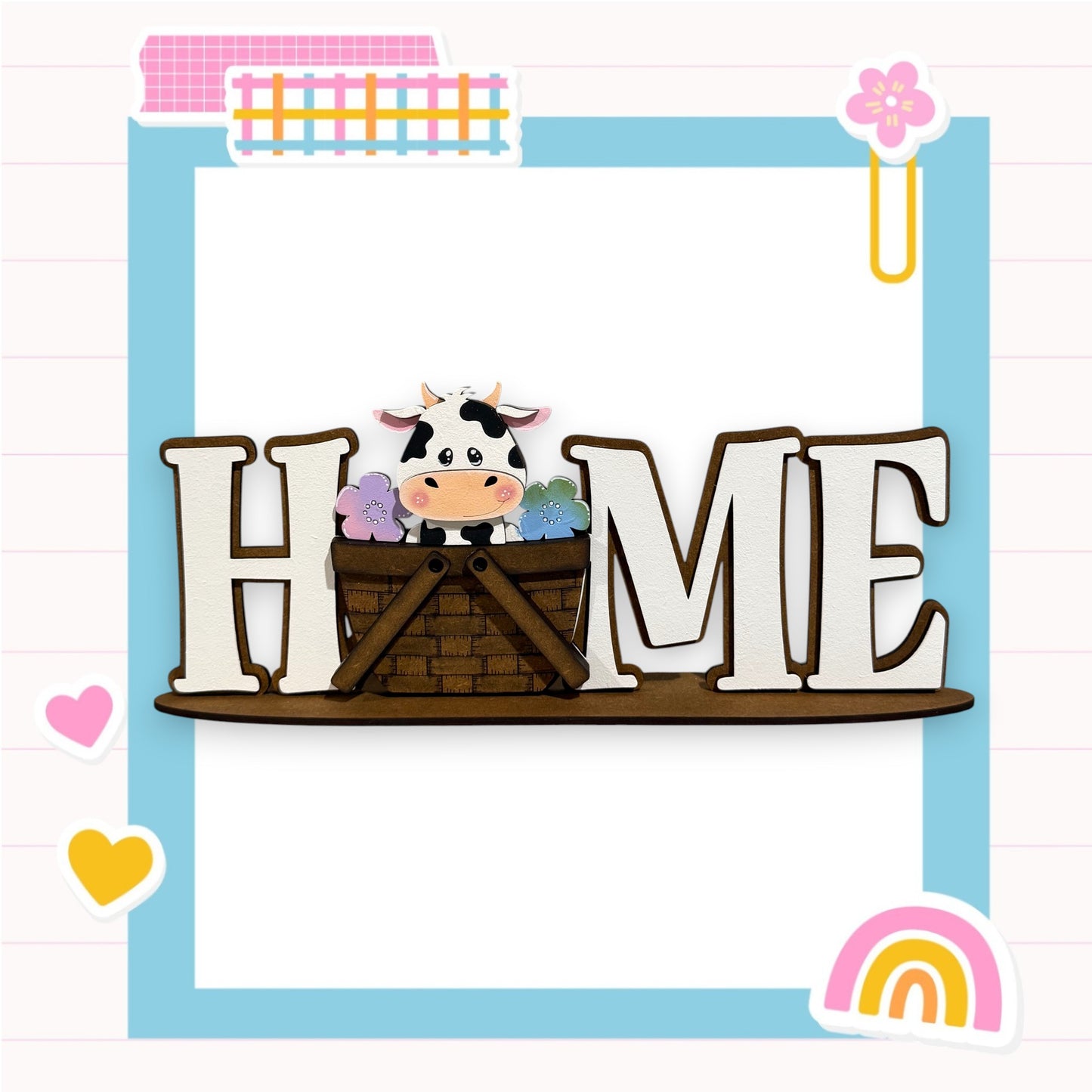 A wooden sign with the word "HOME" in large letters, featuring a cow sitting in a basket. The sign is surrounded by various colorful and whimsical elements, such as hearts, flowers, and a rainbow.