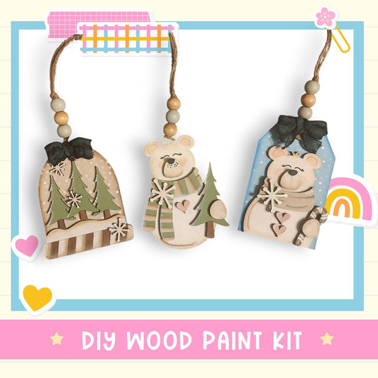 three wooden ornaments hanging from strings, each with a unique design and color. The text "DIY WOOD PAINT KIT" is displayed at the bottom of the image.