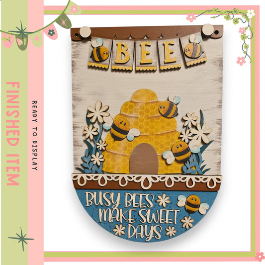 A wooden sign with the word "BEE" and a bee illustration, surrounded by flowers and decorative elements.